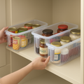 Three clear stackable kitchen organiser baskets holding jars on a cupboard shelf